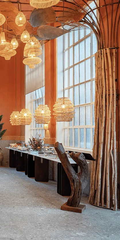 Ambiente da Casa Buriti com mesa comunitária, luminárias de ráfia e tronco escultórico