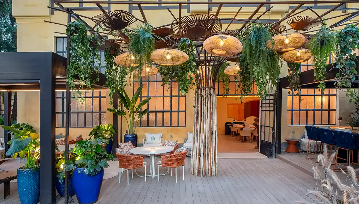 Área externa da Casa Buriti com pergolado, plantas suspensas e mobiliário de fibra