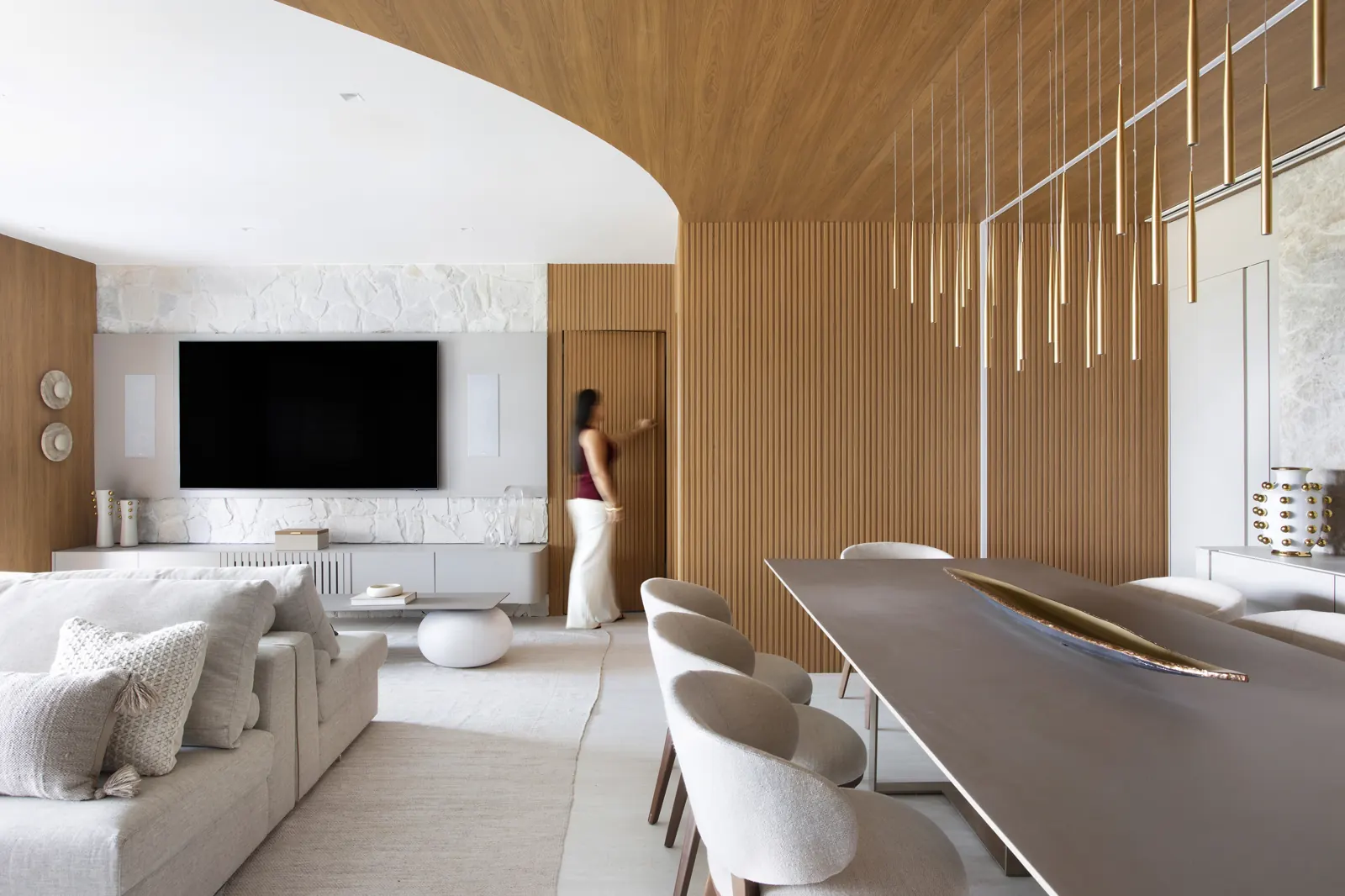 Living amplo com madeira curva, mesa de jantar com pendentes dourados e estante de bronze