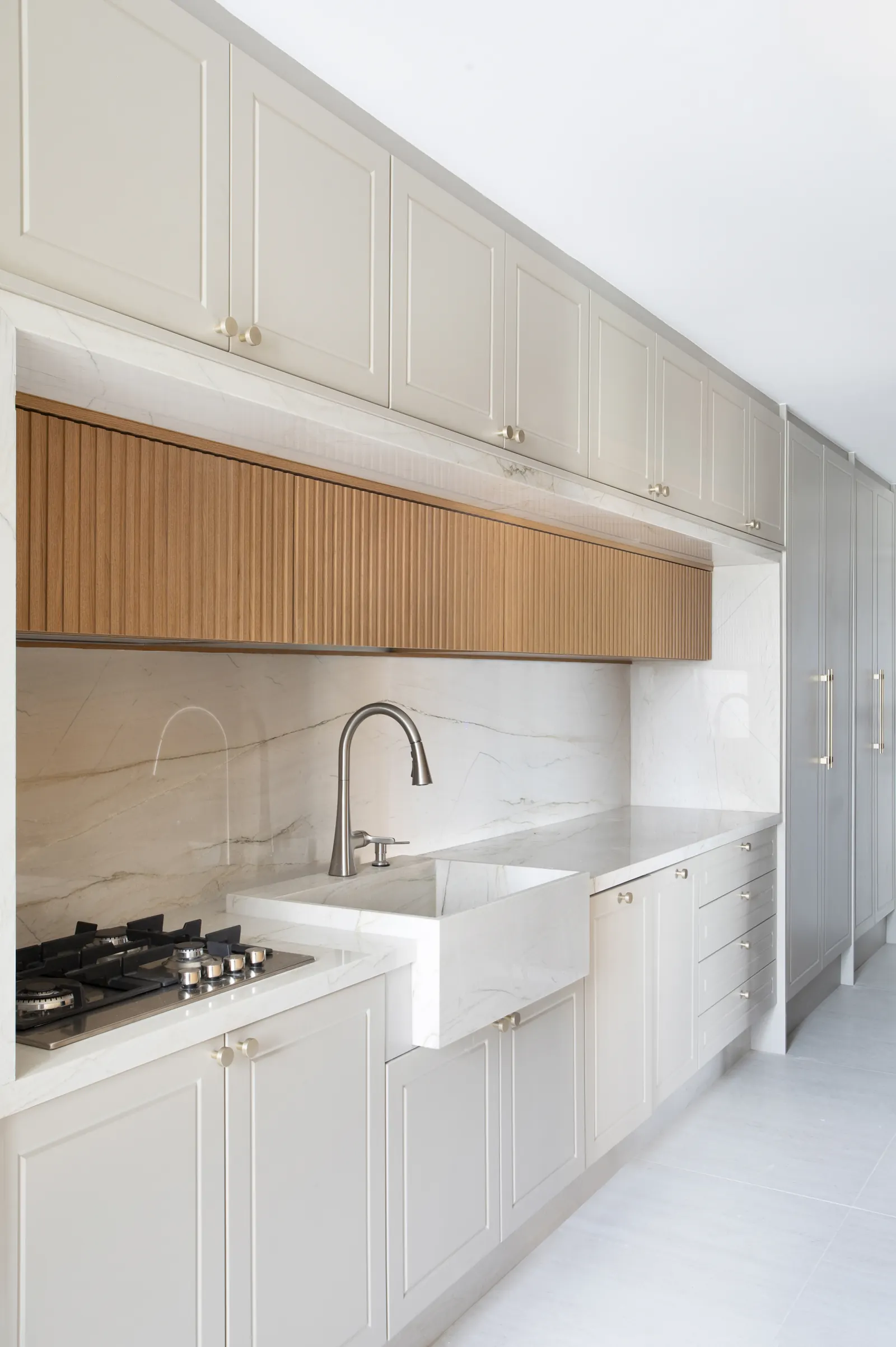 Cozinha com bancada em mármore branco, marcenaria off-white e detalhes em bronze