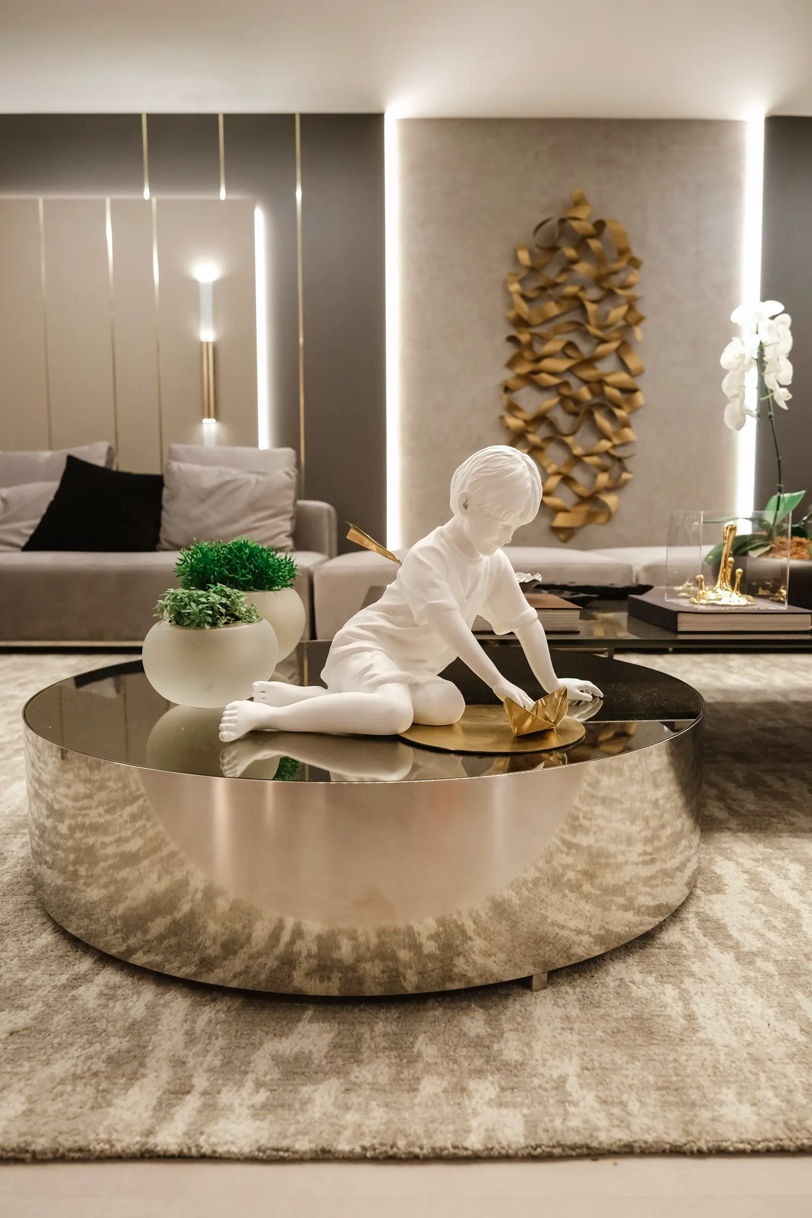 Ambiente com escultura sobre mesa espelhada e painel de arte dourado